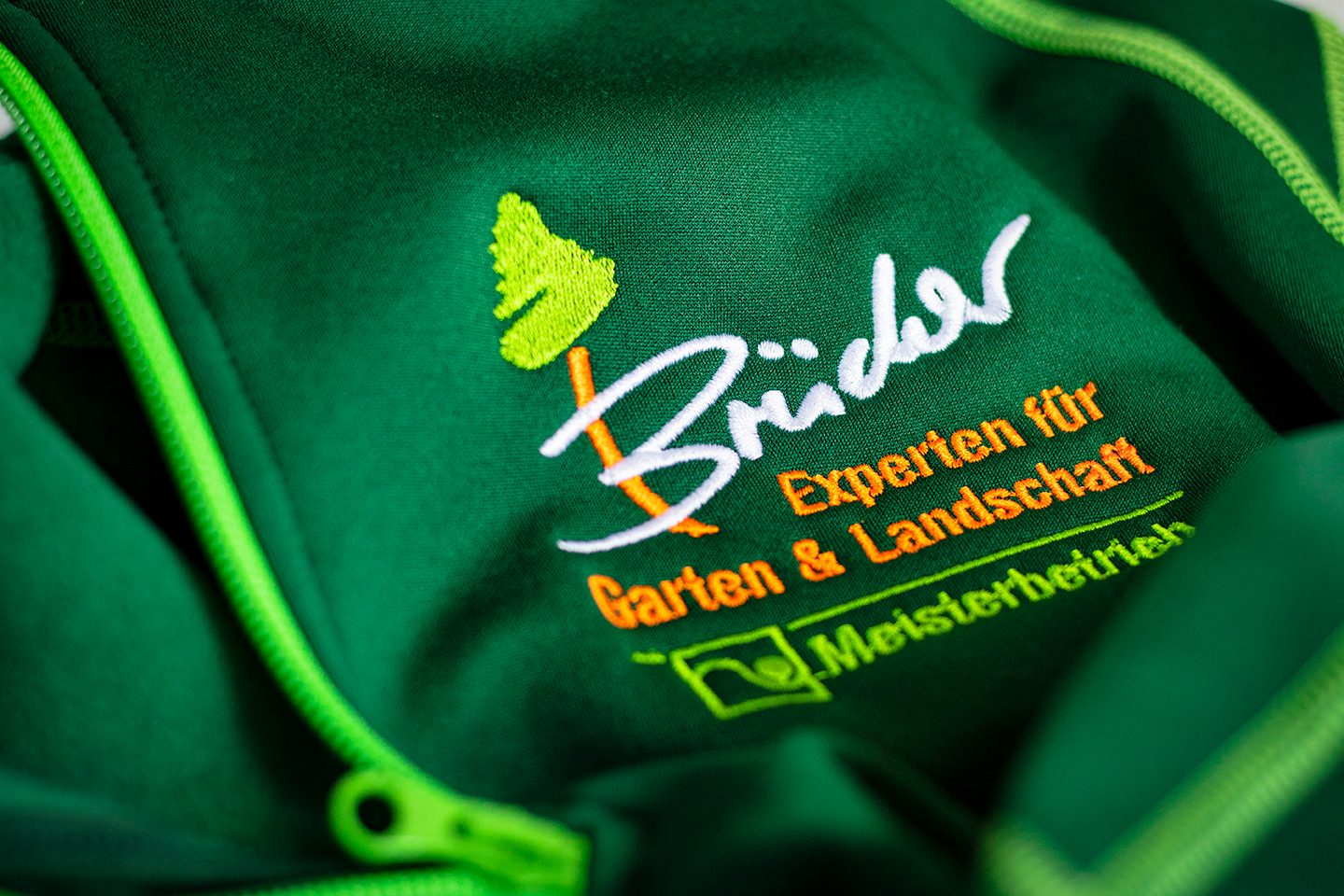 Grüne Softshell-Jacke mit gesticktem Logo eines Garten- und Landschaftsbaubetriebs